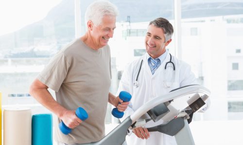 Senior man on treadmill with therapist in fitness studio